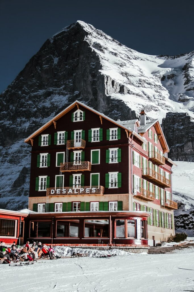 a large brown building with green shutters in front of a snow covered mountain